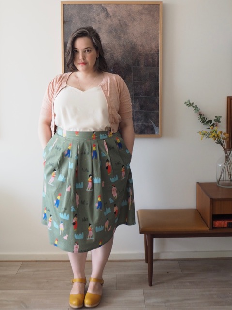 Woman wearing a white singlet, pink cardigan and printed green skirt