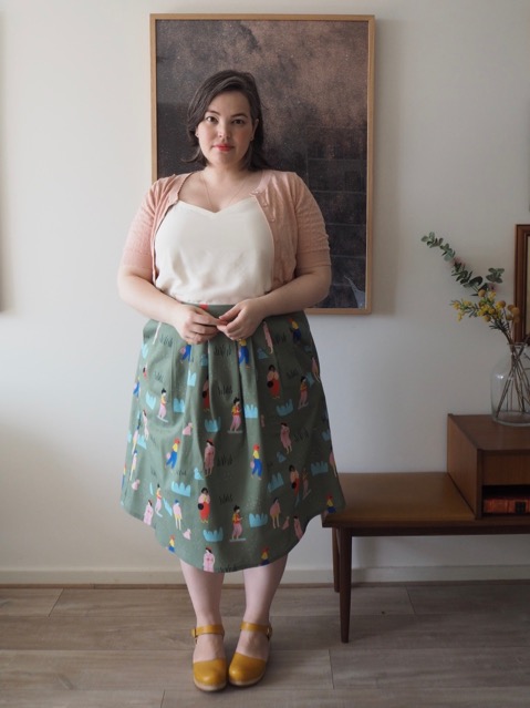 Woman wearing a white singlet, pink cardigan and printed green skirt