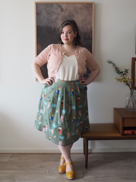 Woman wearing a white singlet, pink cardigan and printed green skirt