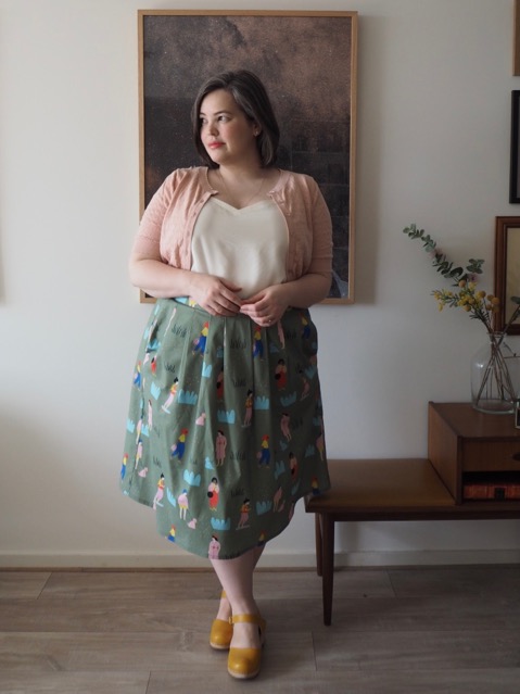 Woman wearing a white singlet, pink cardigan and printed green skirt